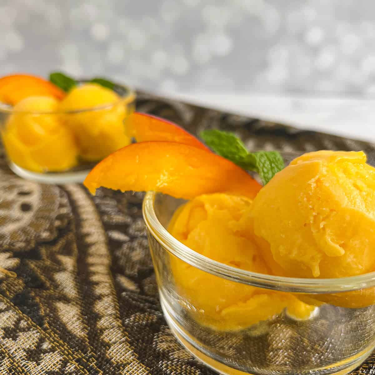 Scoops of Mango Sorbet in glass bowls in foreground & background garnished with mango slices.