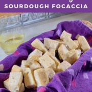 Sourdough Focaccia piled in purple towel lined basket next to a wine glass Pinterest banner.