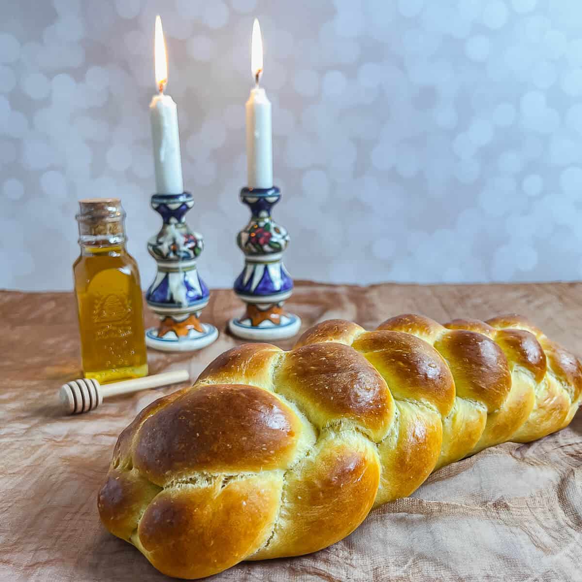 Four strand straight challah with lit candles and a bottle of honey.