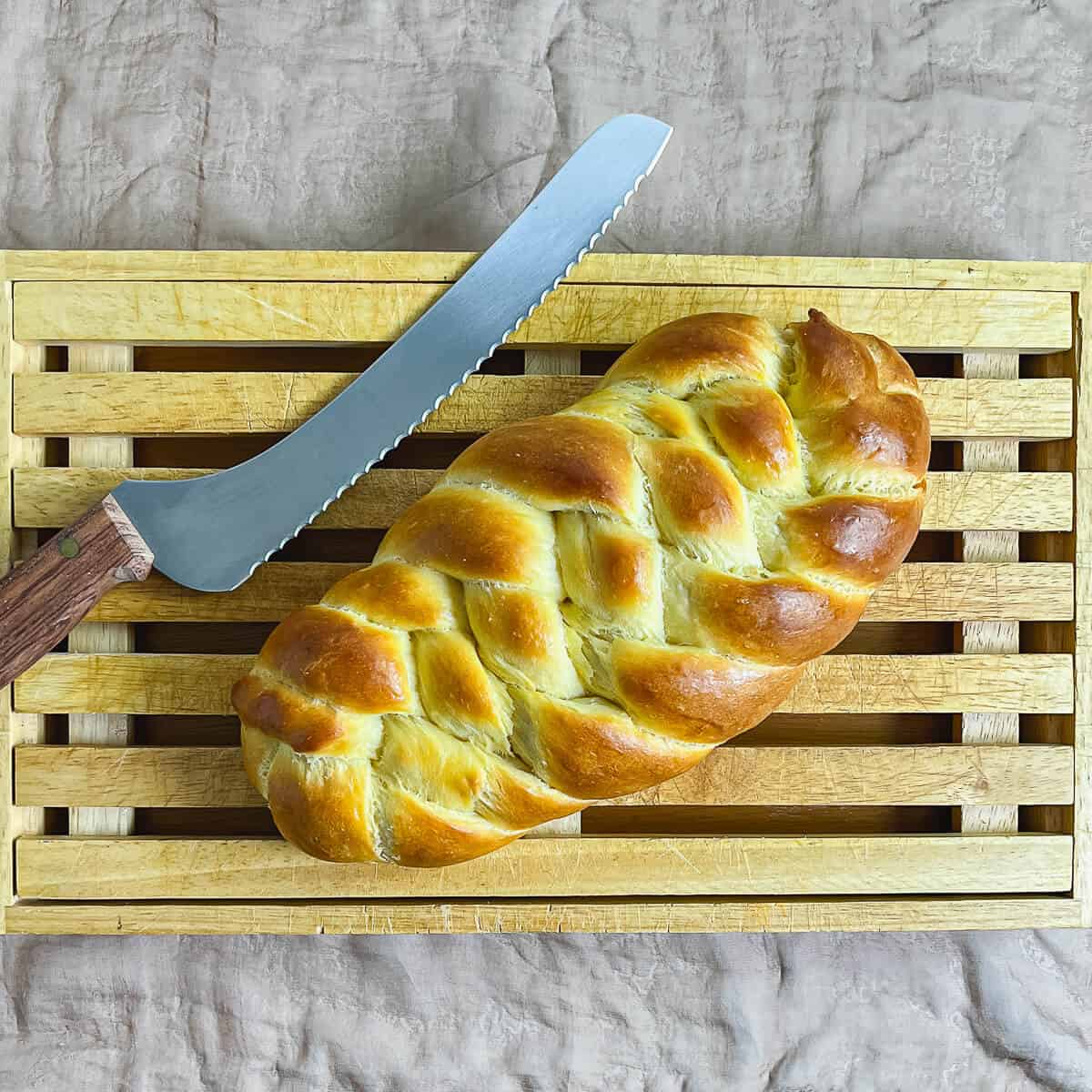 Six strand flat challah on a cutting board with a bread knife.