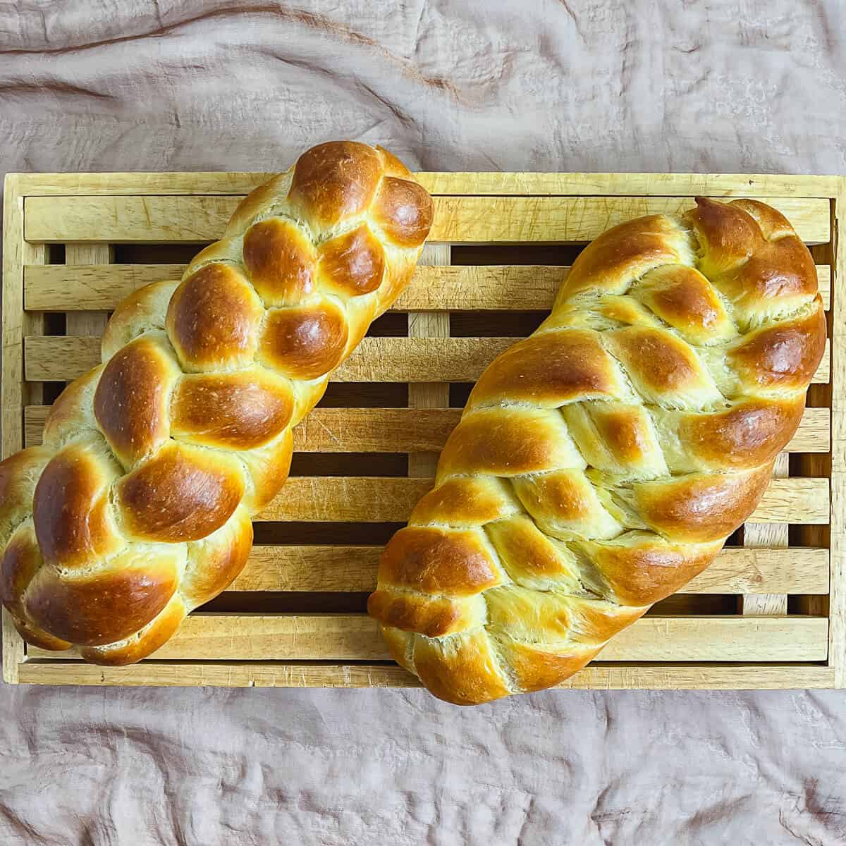 Six strand straight and flat challahs on a cutting board.