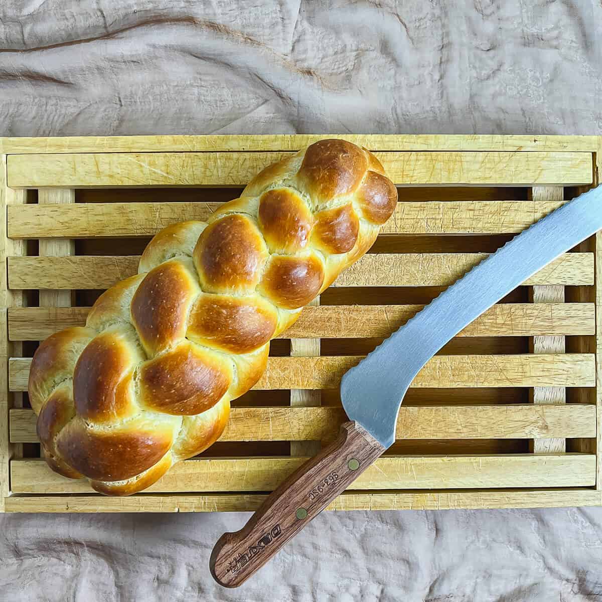 Six strand straight challah on a cutting board with a bread knife.