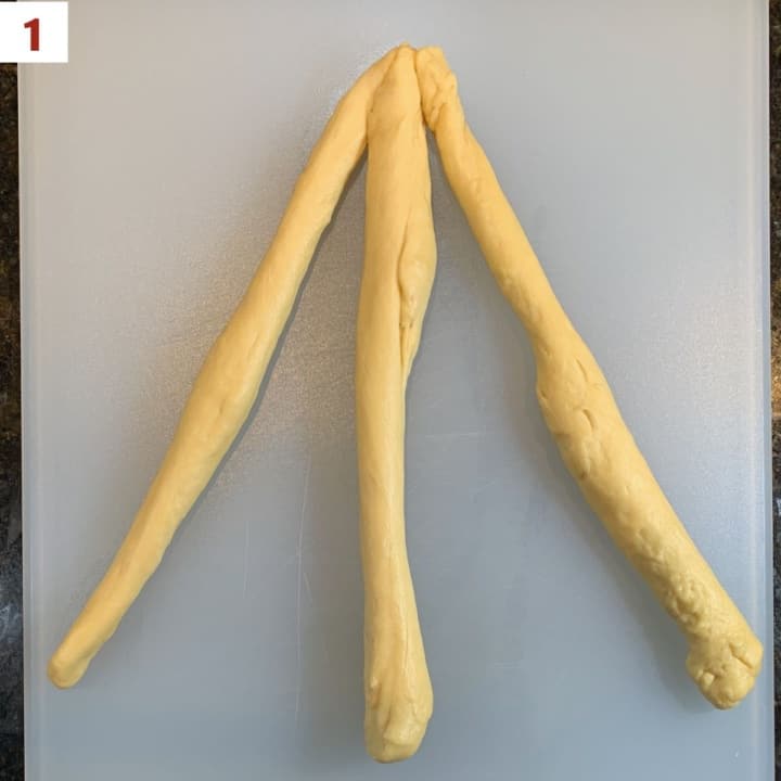Three strands of challah dough lined up side by side & joined at the top.