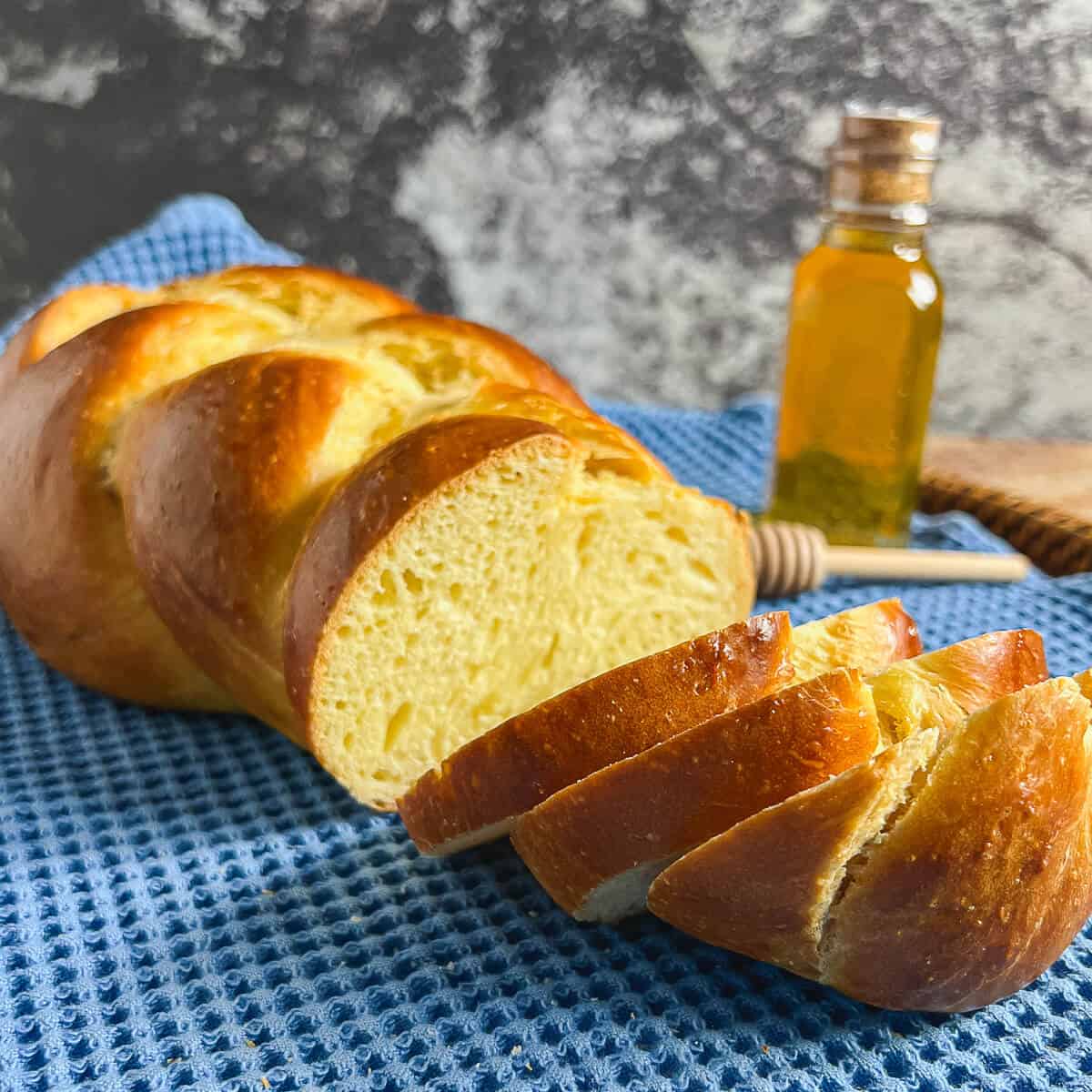 Sliced challah loaf beside a bottle of honey on a blue towel.