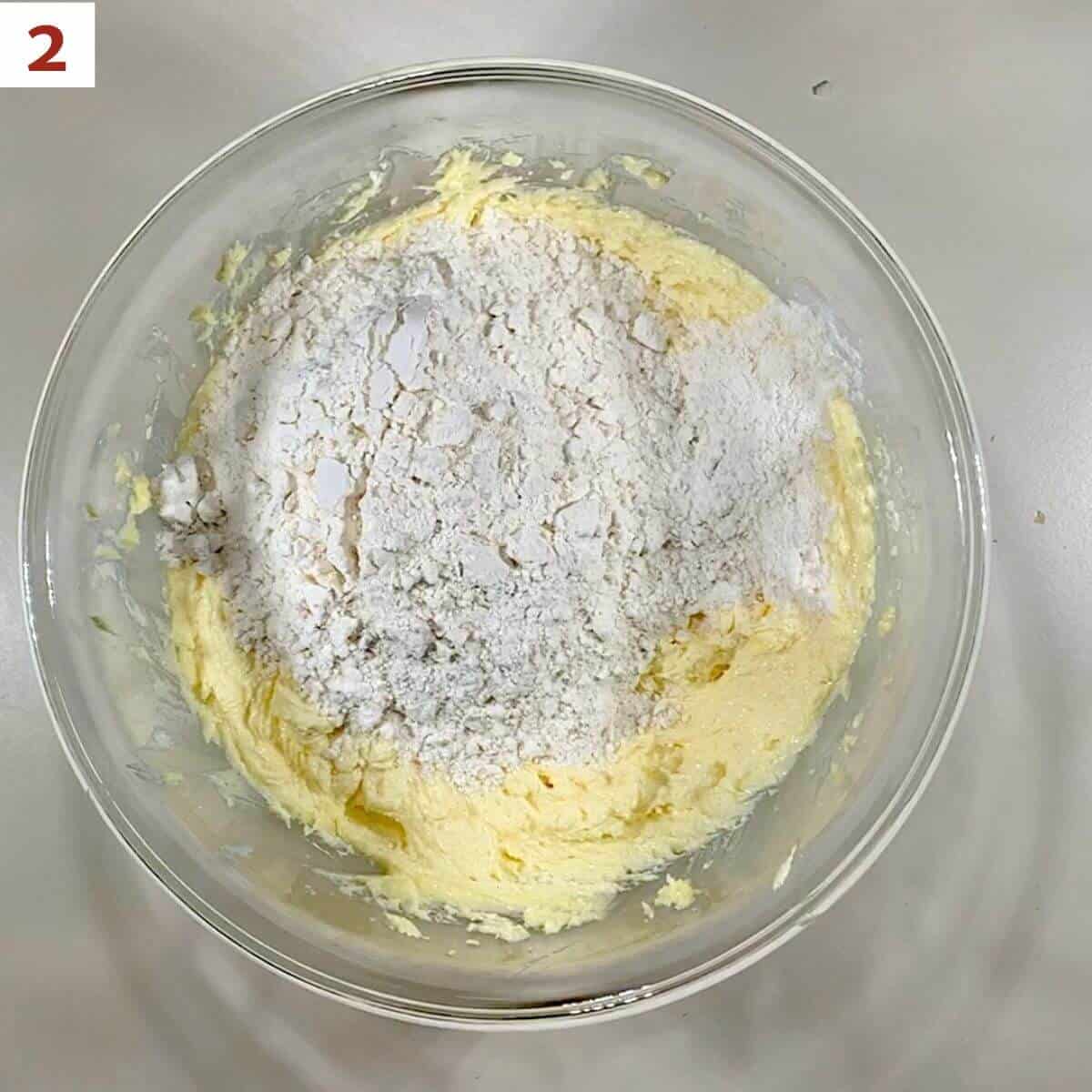 Adding flour to blended butter & sugar in a glass bowl.