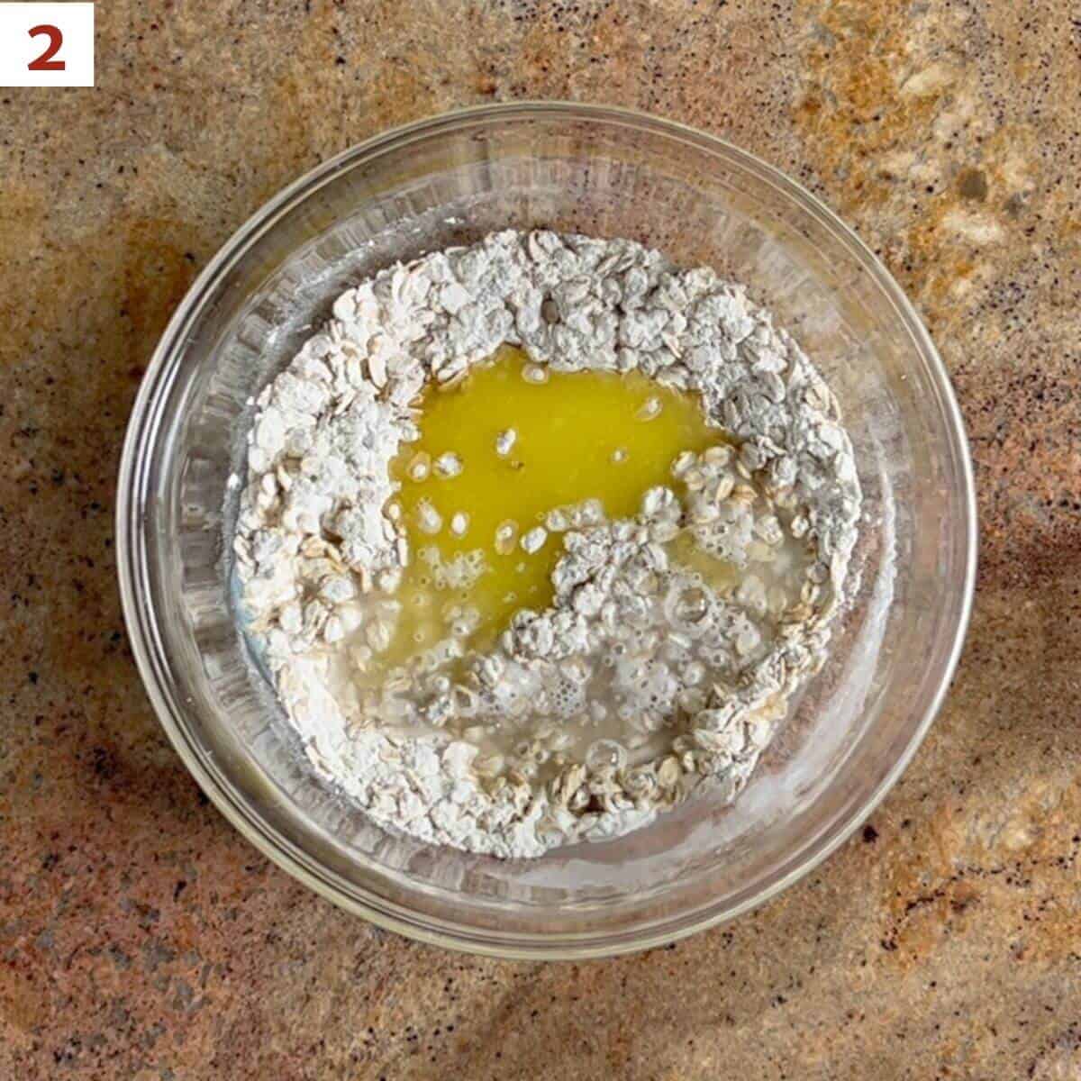 Adding melted butter and water to dry ingredients in a glass bowl.