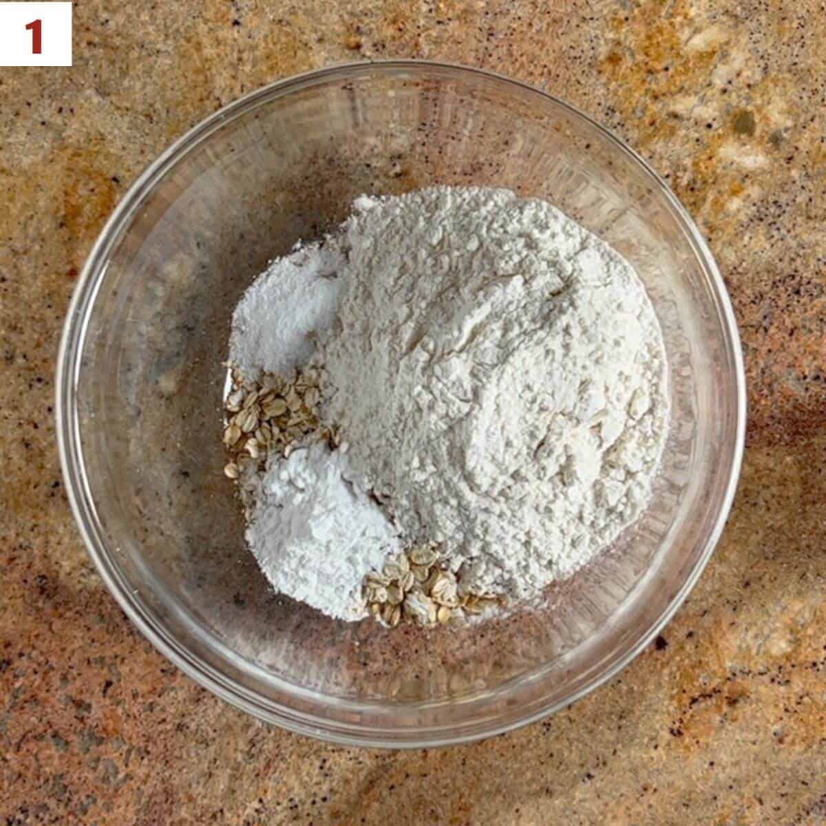 Oats, flour, baking powder, & salt in a glass bowl from overhead.