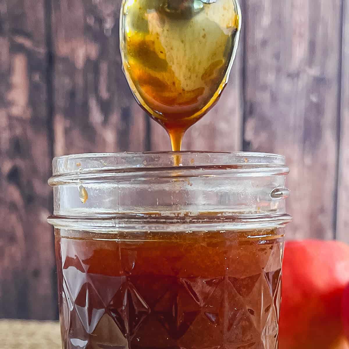 Boiled apple cider dripping from a spoon into a glass jar.