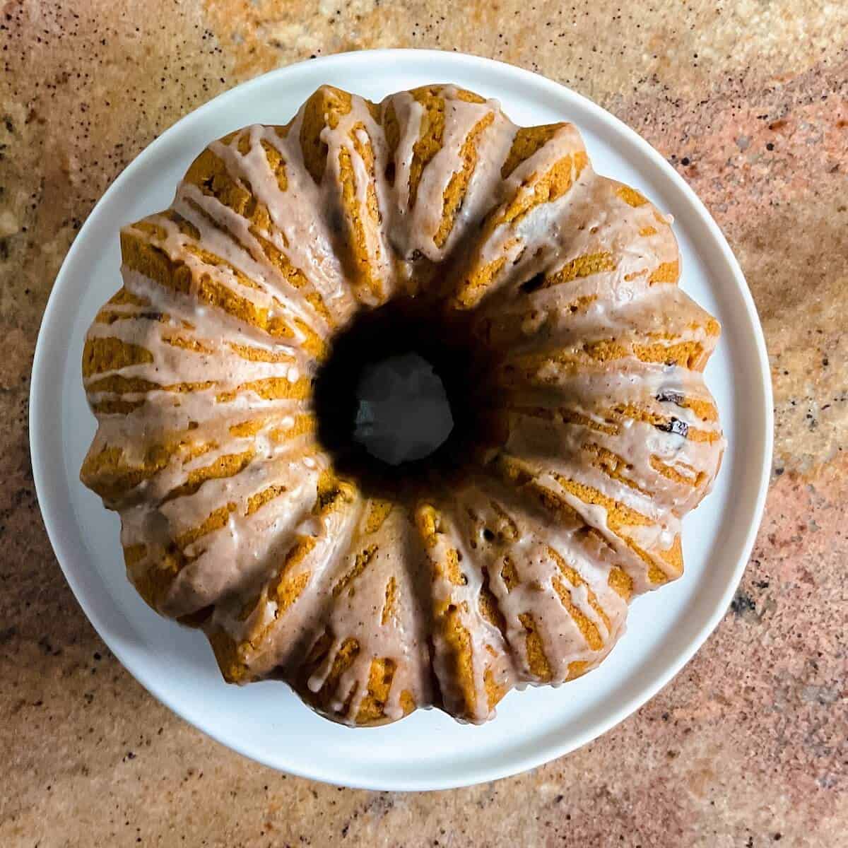 Whole glazed sourdough pumpkin cake on a white cake stand from overhead.