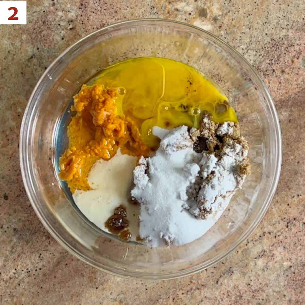 Pumpkin, starter discard, eggs, sugar, brown sugar, oil, and vanilla in a glass bowl from overhead.