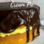 Boston Cream Pie on a white cake stand with plates & forks behind Pinterest banner.