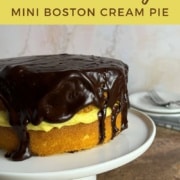 Boston Cream Pie on a white cake stand with plates & forks behind Pinterest banner.