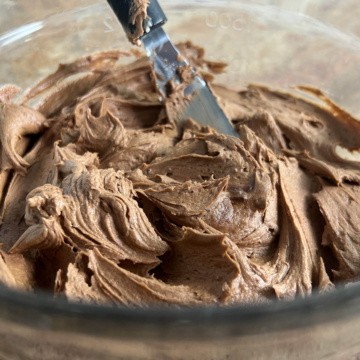 Bowl of dark chocolate buttercream frosting with an offset spatula sticking out.