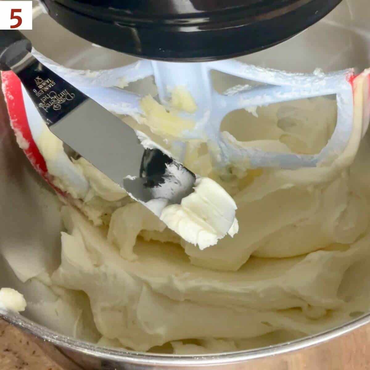 Creamy vanilla buttercream shown on an small offset spatula over a stand mixer bowl of frosting.