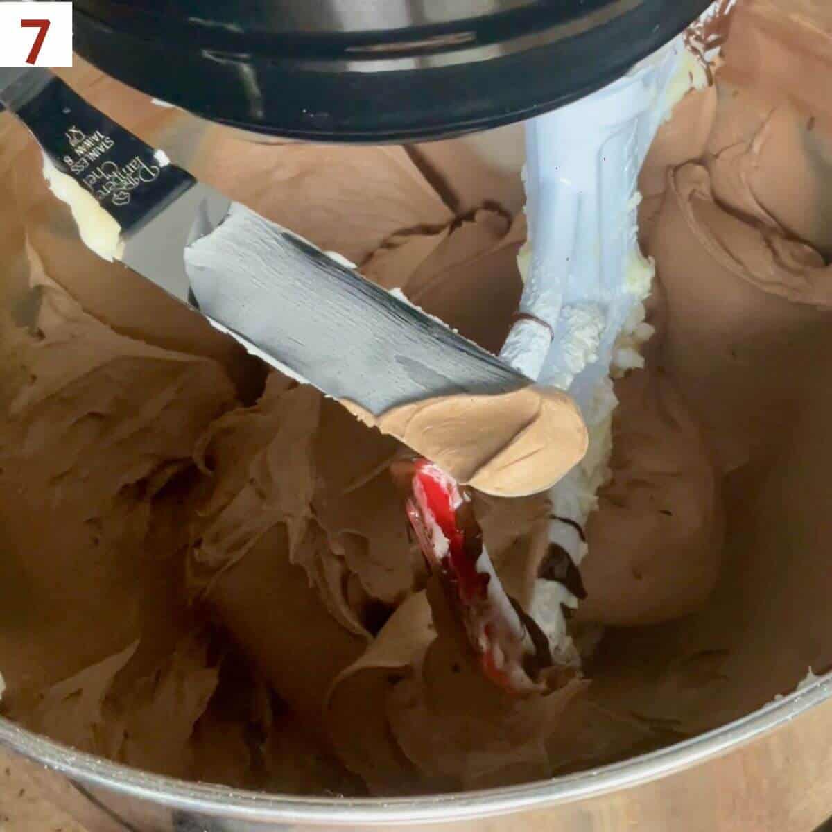 Dark chocolate buttercream shown on an small offset spatula over a stand mixer bowl of frosting.