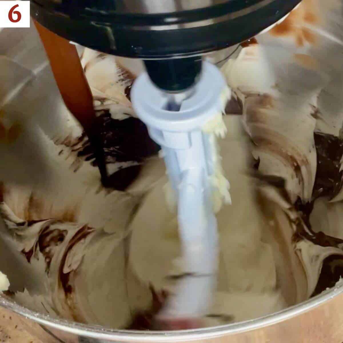 Adding melted chocolate to buttercream in a stand mixer bowl.