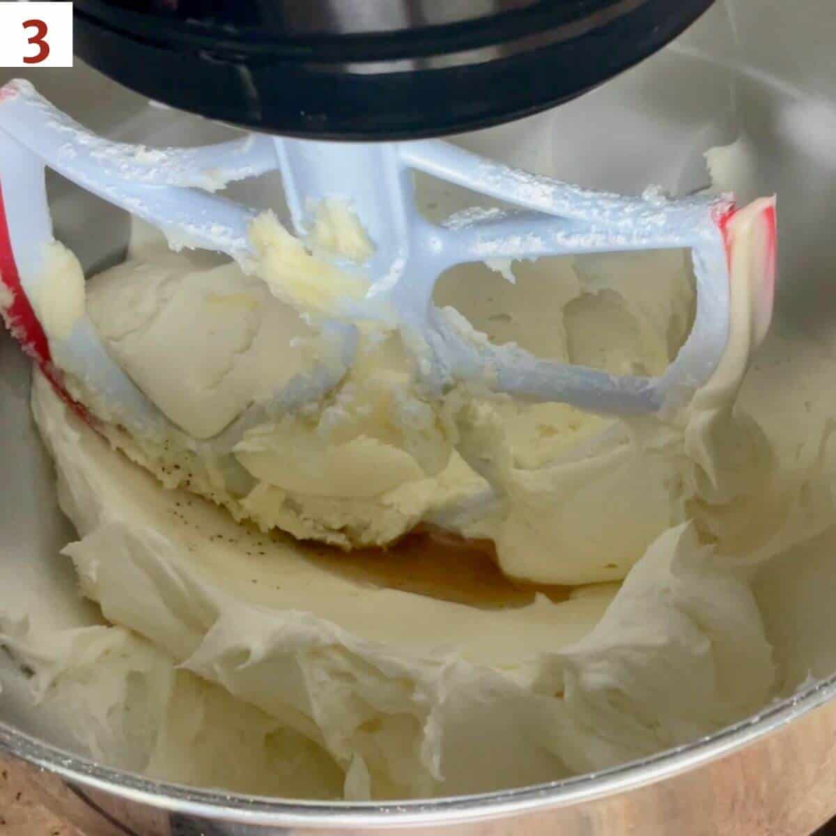 Adding vanilla to buttercream in a stand mixer bowl.