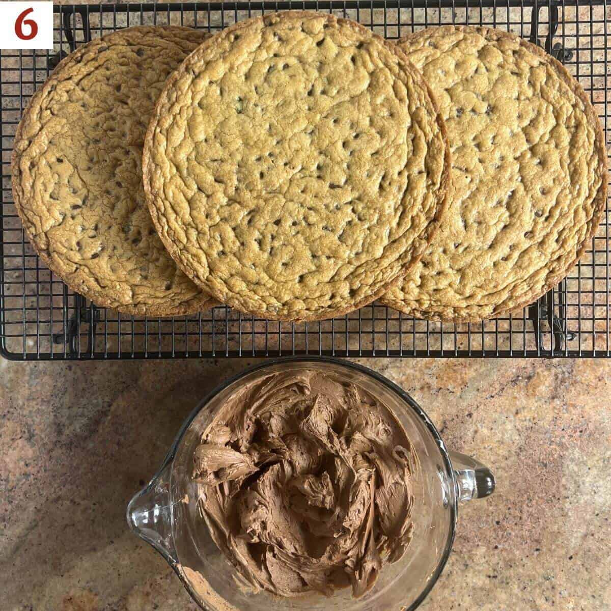 Cake layers on a cooling rack next to a bowl of chocolate frosting from overhead.