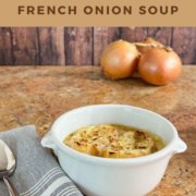 French Onion Soup in a bowl next to a spoon on a grey napkin with onions behind Pinterest banner.