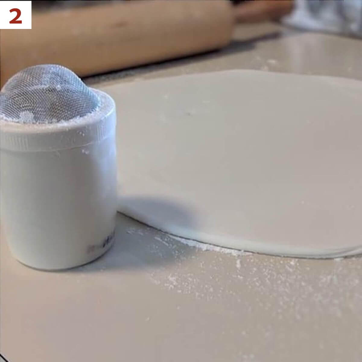 Marshmallow fondant rolled out next to a powdered sugar shaker.