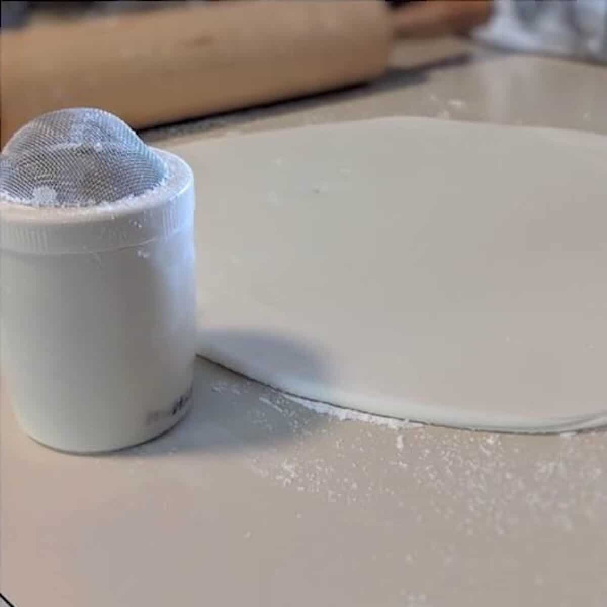 Marshmallow fondant rolled out next to a powdered sugar shaker.