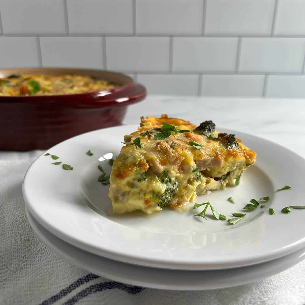 Slice of crustless quiche plated on two stacked round white plates with quiche baking pan behind.