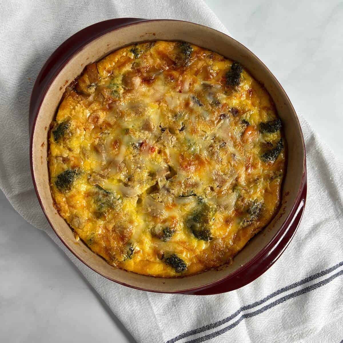 Whole Sausage & Broccoli quiche in a red baking dish on a white towel from overhead.