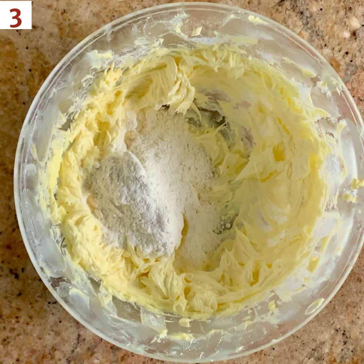 Adding flour to cookie dough in a glass bowl.