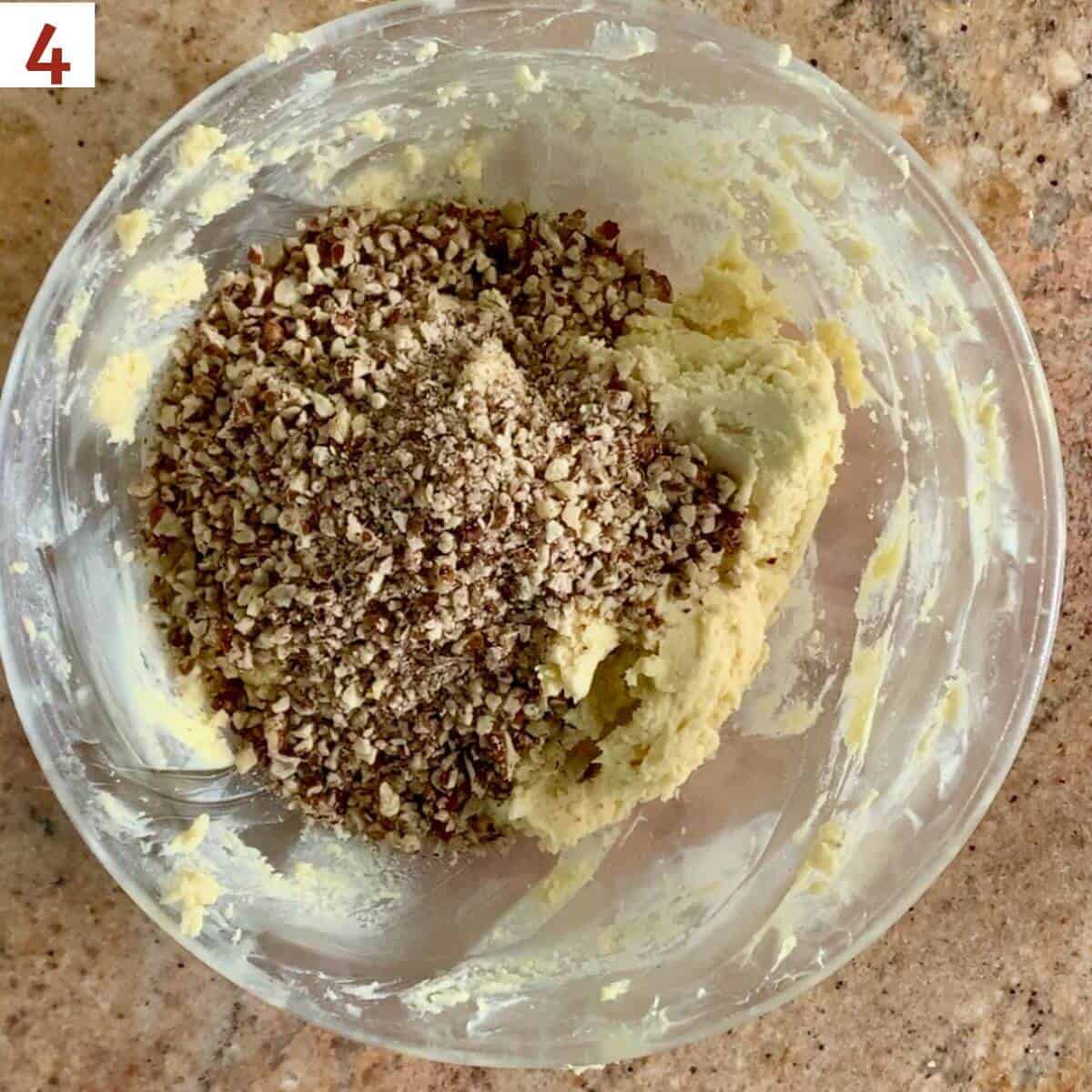 Adding chopped pecans to cookie dough in a glass bowl.