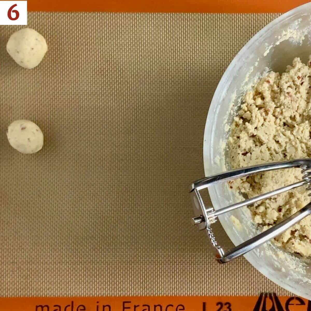 rolled dough balls on a baking pan next to bowl of dough & cookie scoop.