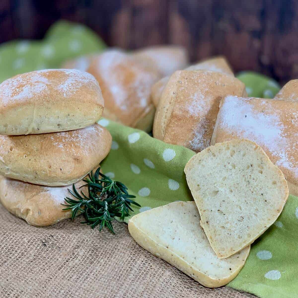 Sourdough Herb Ciabatta Rolls stacked next to a rolls cut open with rolls on a green spotted towel behind.