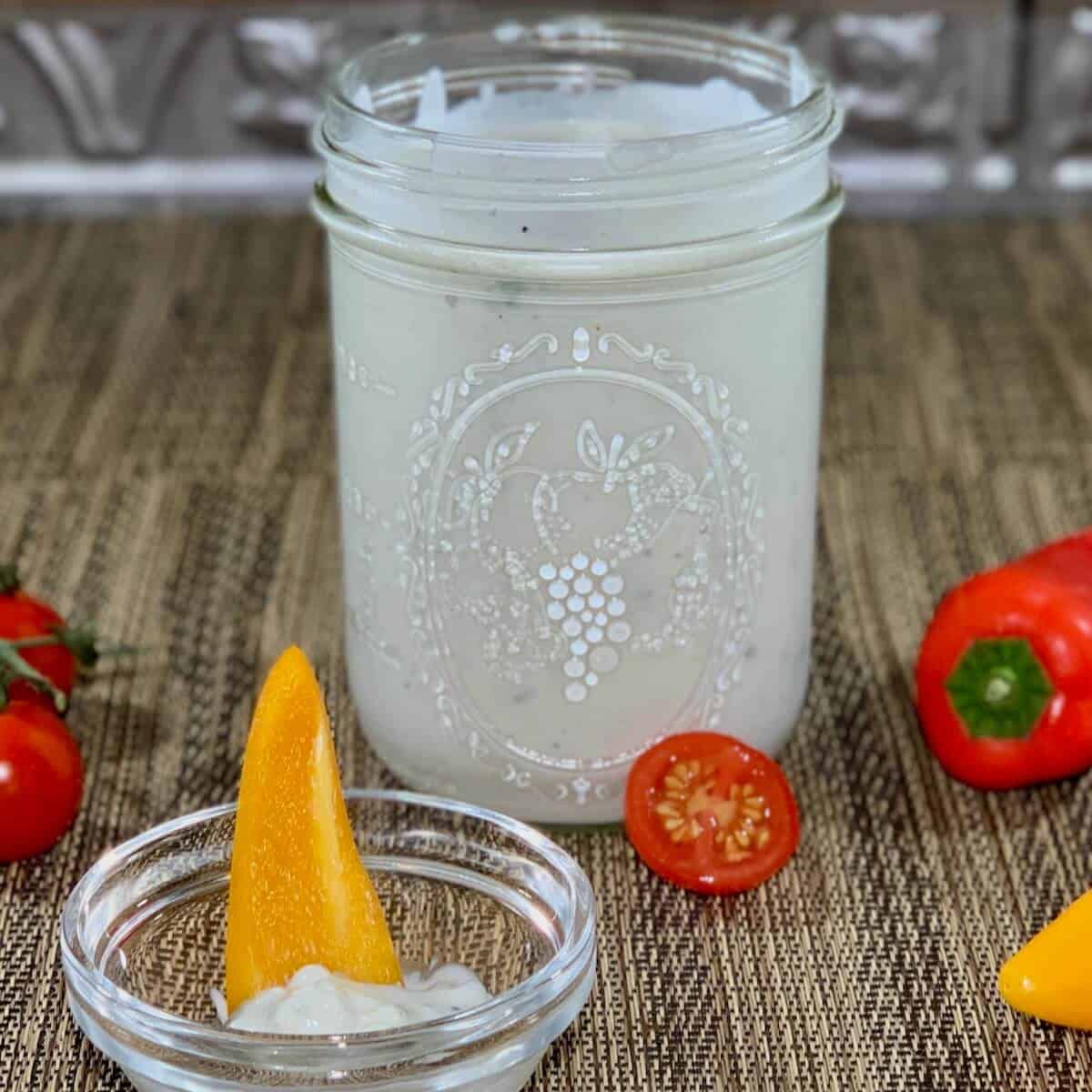 Buttermilk blue cheese dressing in a jar surrounded by tomatoes & cut bell peppers.