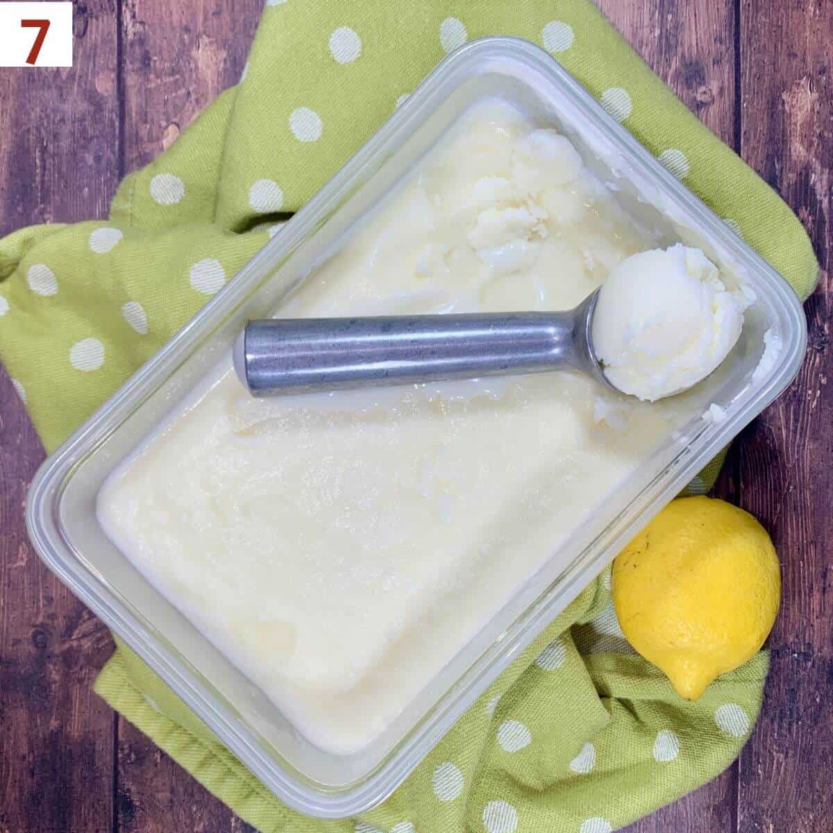 Lemon Sherbet scooped in container with green towel & lemon on a wood backdrop.