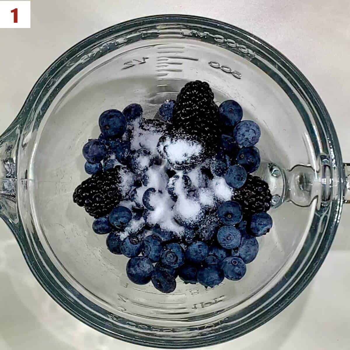 Blueberries & blackberries with sugar in a glass bowl from overhead.