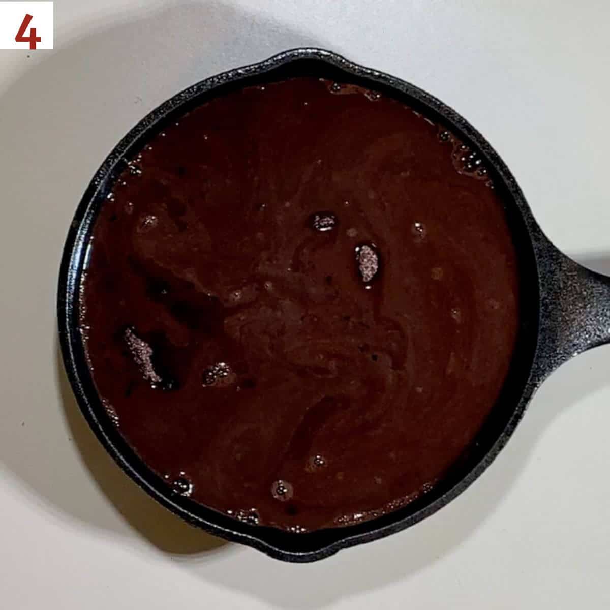 Hot water poured over pudding cake in a mini skillet from overhead.