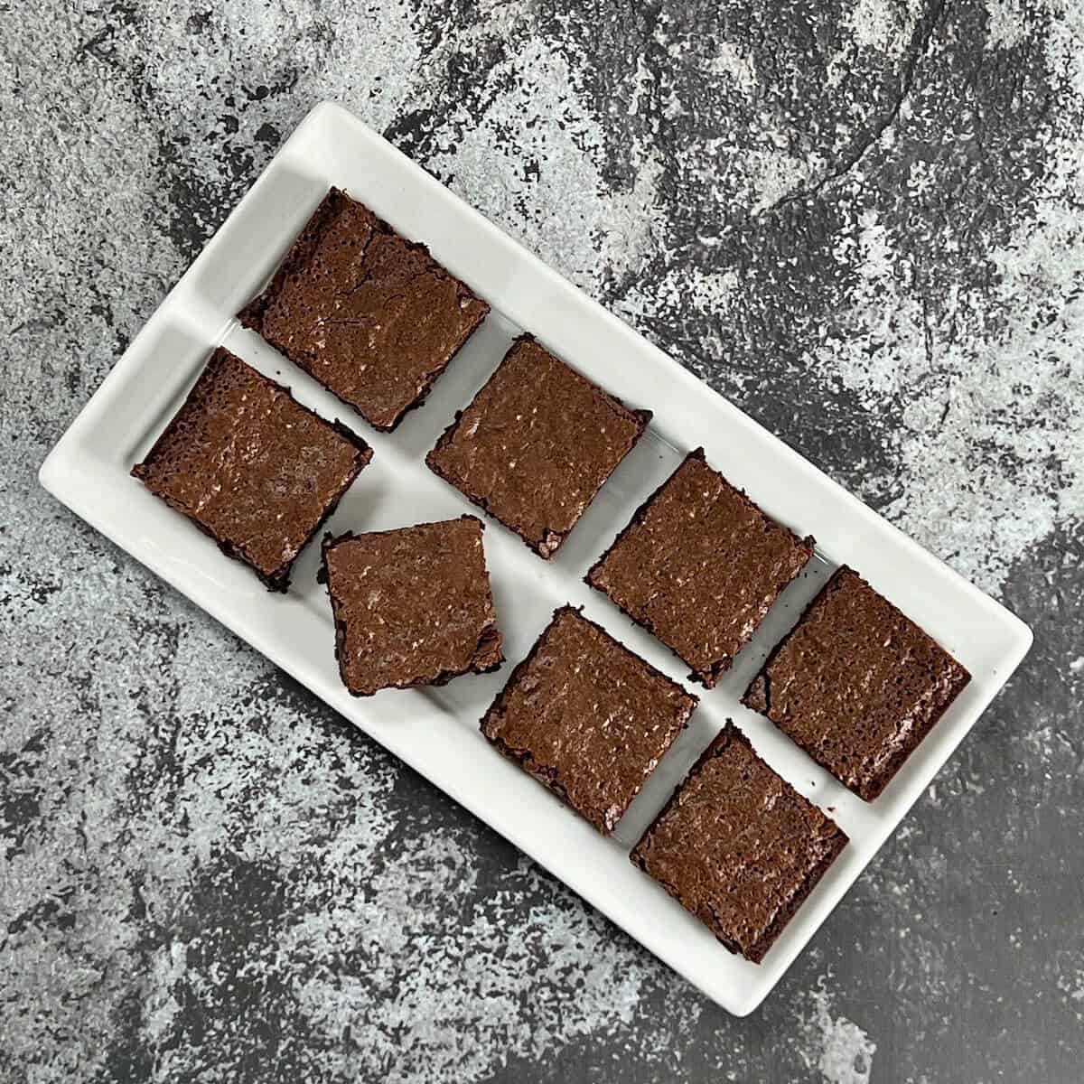 Two rows of four bourbon brownies lined up on a diagonally-placed white rectangular plate with on turned diagonally from overhead.