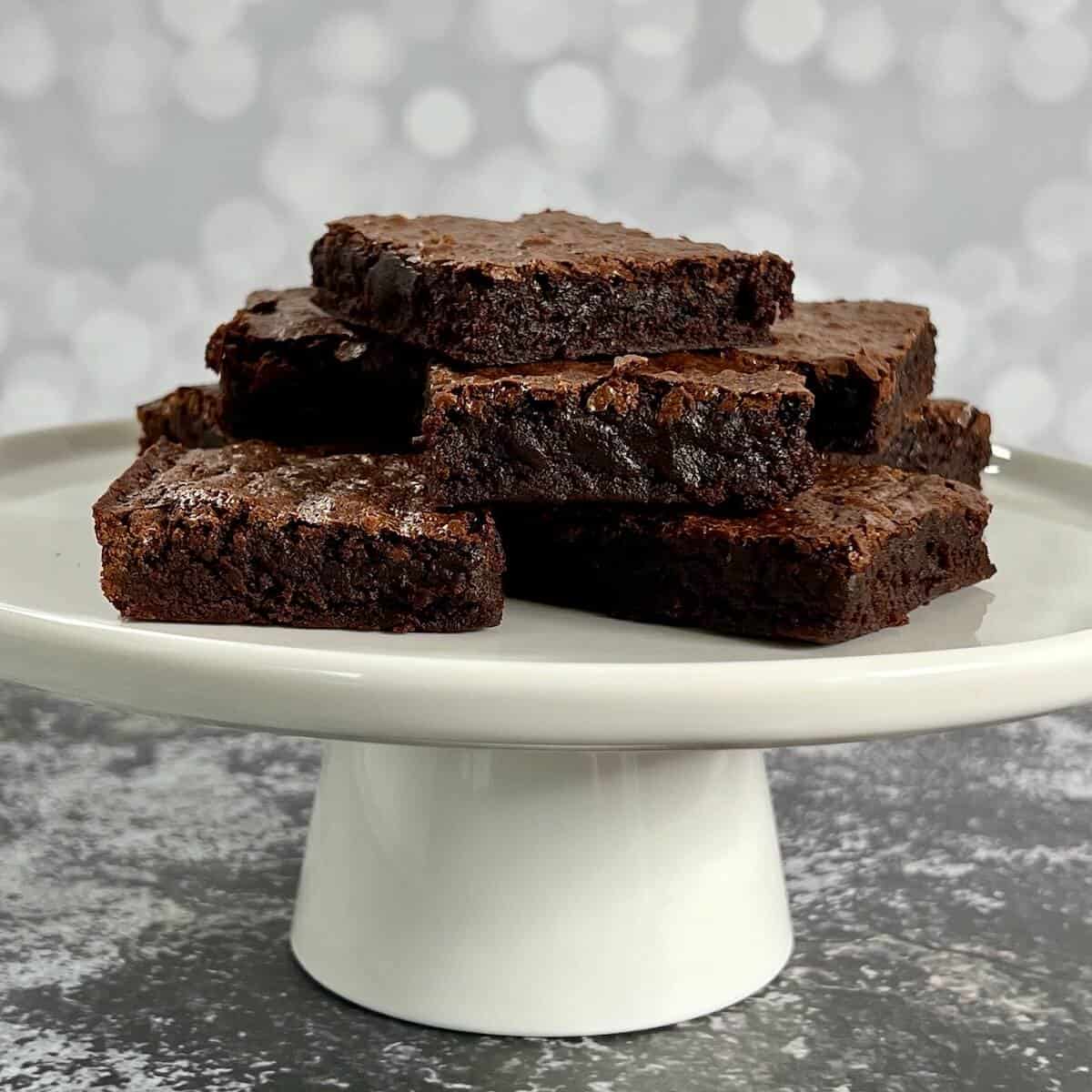 Stack of bourbon brownies on a white cake stand.