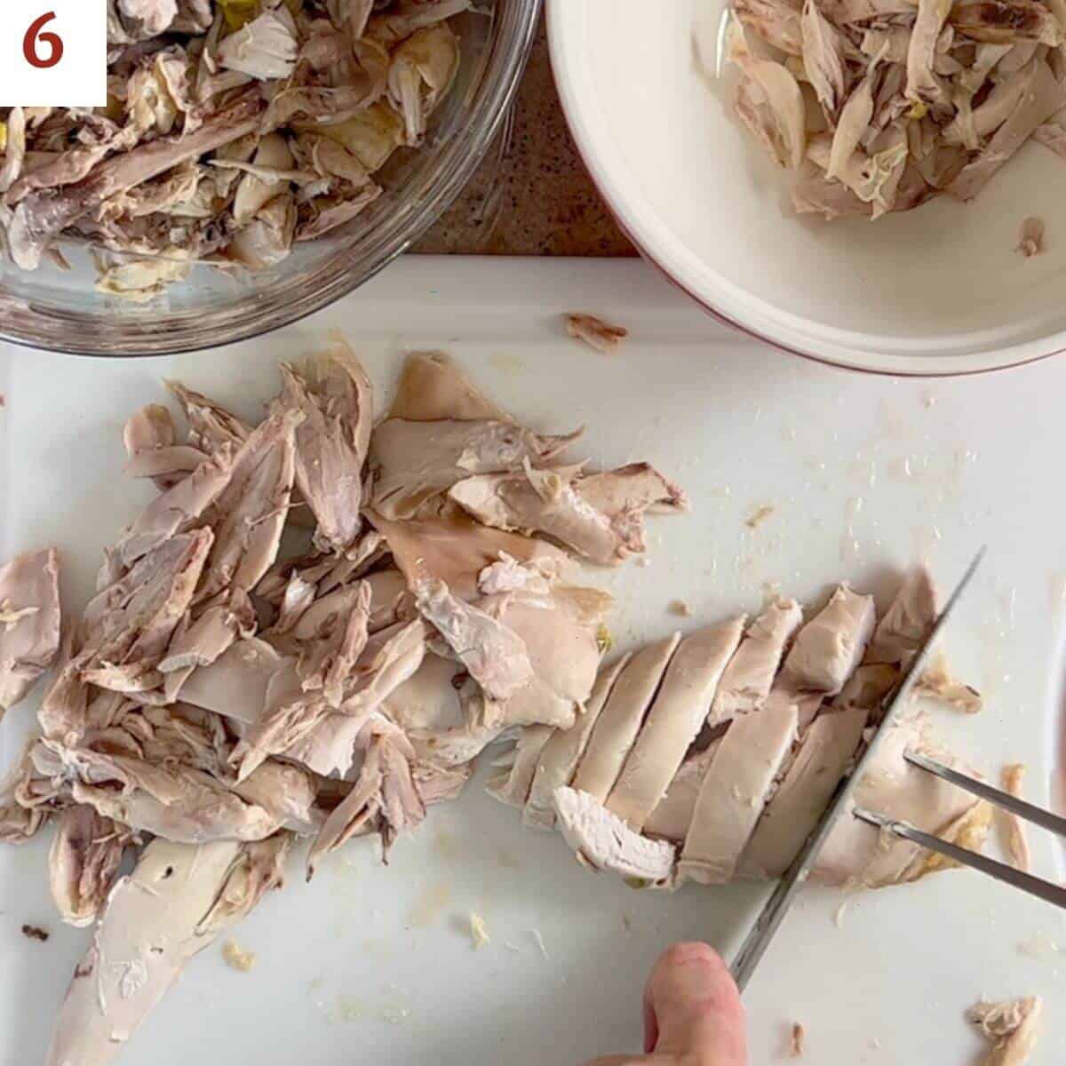 Cutting up cooked chicken breast on a white cutting board.