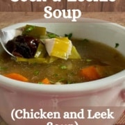 Cock-a-leekie soup in a white bowl with a spoon lifting prunes and leeks all on a red checkered towel Pinterest banner.