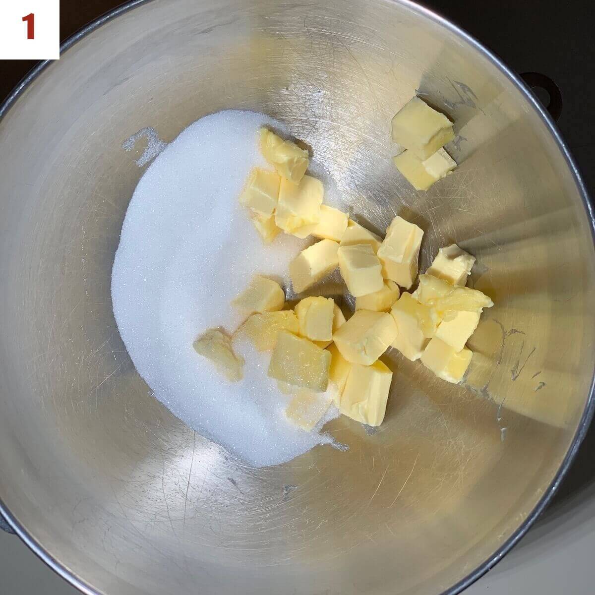 Cubed butter and sugar in a metal mixing bowl from overhead.