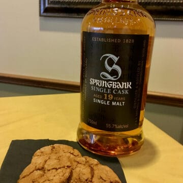 Bottle of Springbank Single Cast on a yellow tablecloth next to 3 molasses cookies on a black napkin.