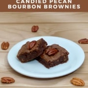 Two candied pecan bourbon brownies on a white plate surrounded by whole pecans Pinterest banner.