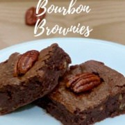 Two candied pecan bourbon brownies on a white plate surrounded by whole pecans Pinterest banner.