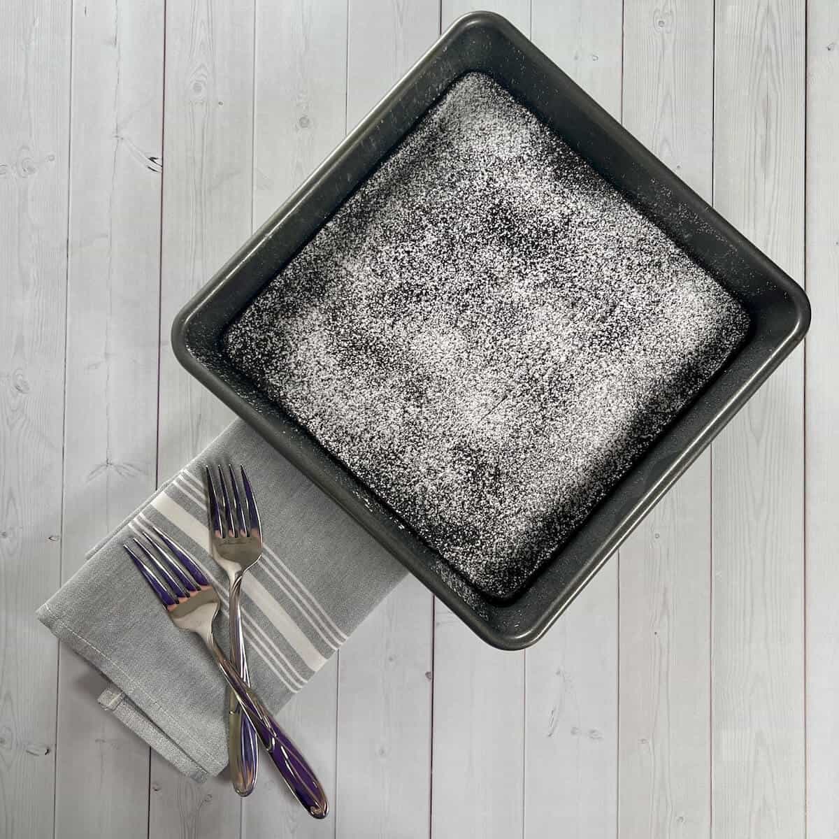 Whole eggless chocolate cake in the pan with two forks from overhead.