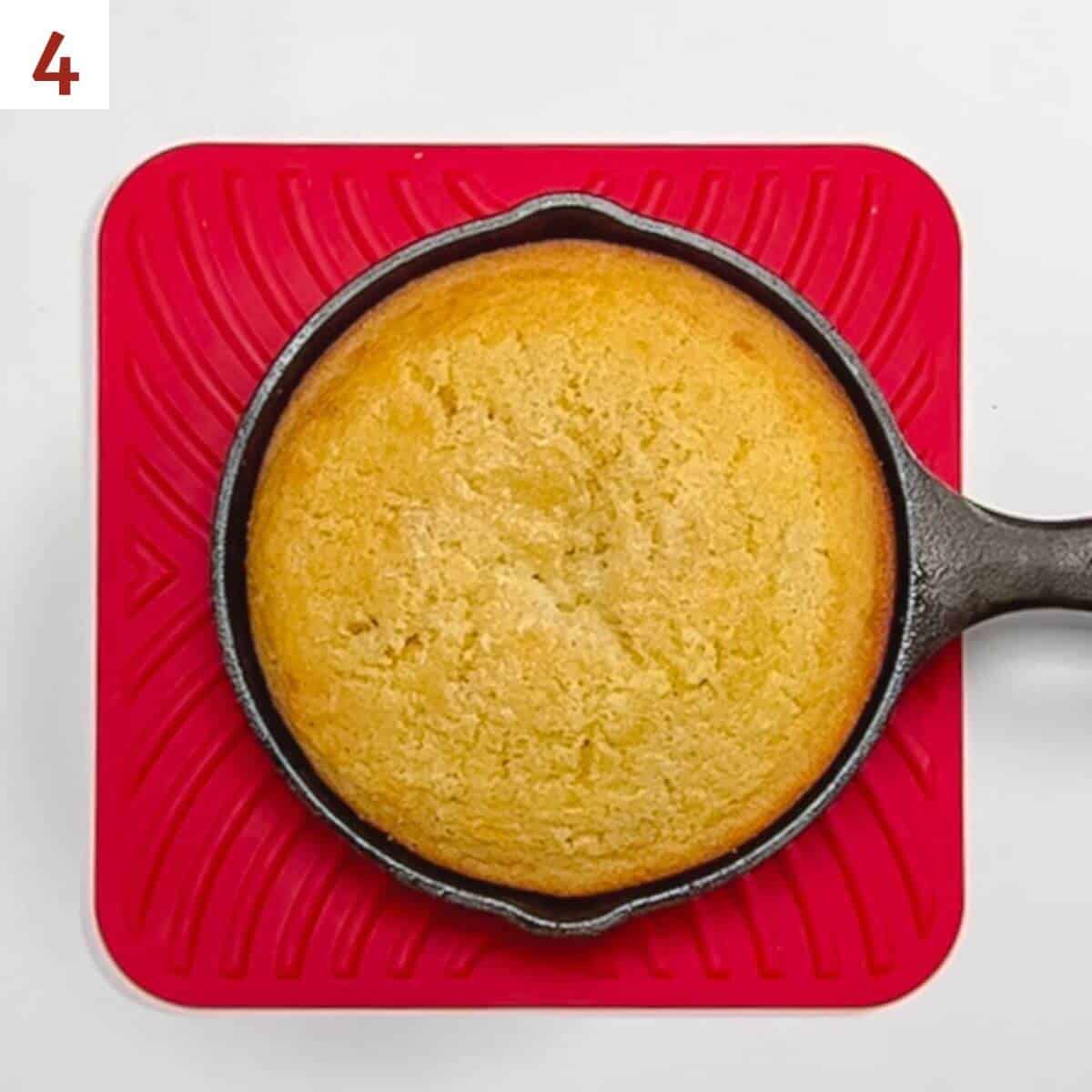 Baked cornbread in a cast iron skillet on a red trivet from overhead.
