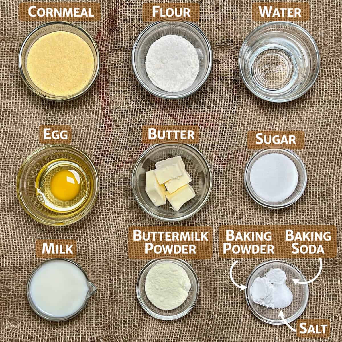 Ingredients for skillet cornbread portioned into glass bowls on a piece of burlap from overhead.