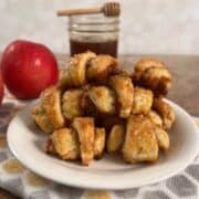 Apple Cinnamon Rugelach stacked on a white plate in front of an apple and a jar of boiled cider.