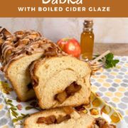 Sliced apple honey babka on a plate with an apple and honey in a jar and bowl behind all on a honeycomb-decorated towel Pinterest banner.