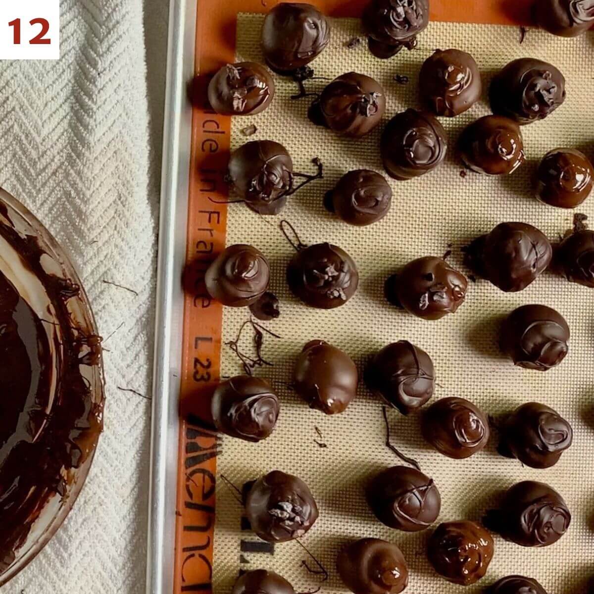 Dipped chocolate truffles drying on baking pan lined with a Silpat silicone mat.