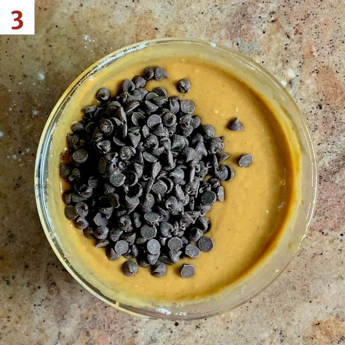 Adding chocolate chips to pumpkin bread batter in a glass bowl.